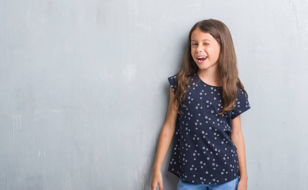 Молода іспаномовна дитина над гранжевою сірою стіною підморгує дивитися на камеру з сексуальним виразом, веселим і щасливим обличчям
. - Фото, зображення