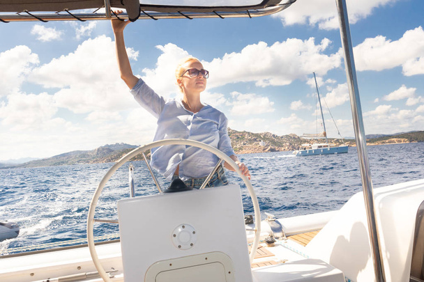 Atraktivní blondýna ženské kapitán navigaci luxusní katamarán plachetnice ve slunečný letní den na klidné modré mořské vody. - Fotografie, Obrázek
