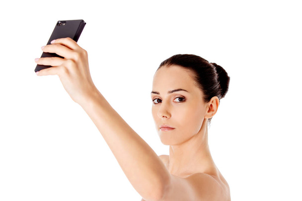 Nude beautiful woman taking selfie on white background. - Foto, afbeelding