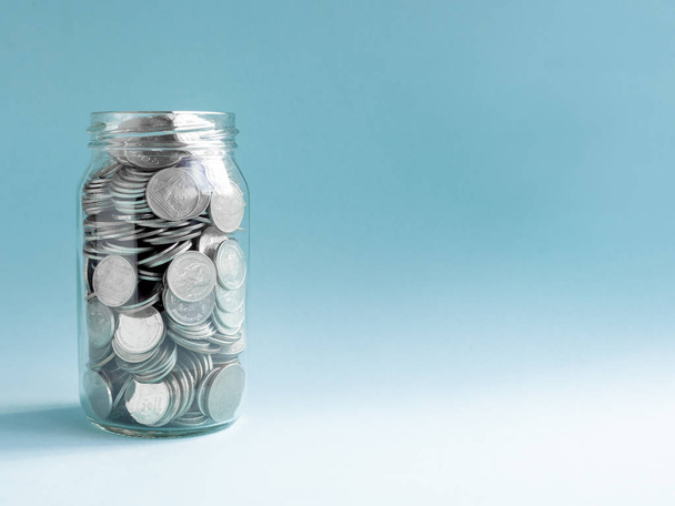 Coins in glass jar isolated on blue background with copy space. Saving money concept. - Foto, Bild