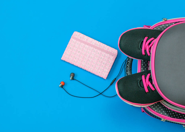 Kids sneakers in school backpack and school supplies on blue background. Child's school accessories. The view from the top. Flat lay. - Photo, Image