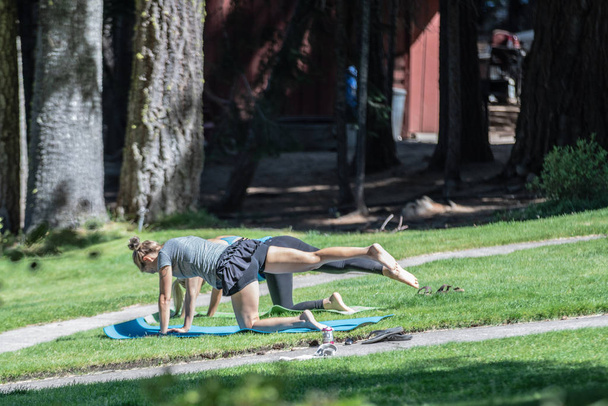 Bend, OR / USA - September 1, 2018: Two young attractive females doing yoga in the public park. - Zdjęcie, obraz