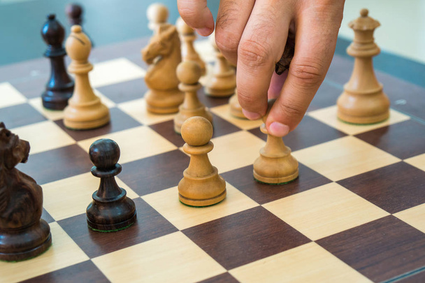 Main déplaçant une figure d'échecs en bois sur un échiquier
. - Photo, image