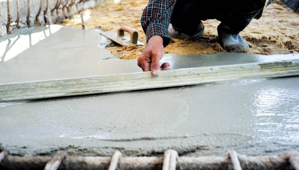 Trabalhador usando espátula de madeira para nivelar o piso de concreto no canteiro de obras
 - Foto, Imagem