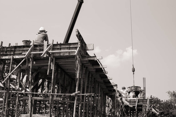 Monochrome de travailleurs transportant le récipient de ciment à verser dans le moule à la maison sous construction. Travail d'équipe et concept d'esprit
 - Photo, image