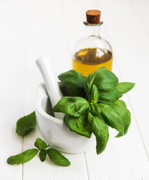 Tuore vihreä basilika ja oliiviöljy valkoisella puupöydällä
 - Valokuva, kuva