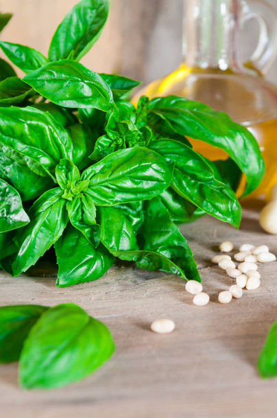 Fresh, green, organic basil on a wooden table. And products for salad: tomatoes, garlic, pine nuts. Photo is made in a rustic style with a blurred background. - Foto, Imagen