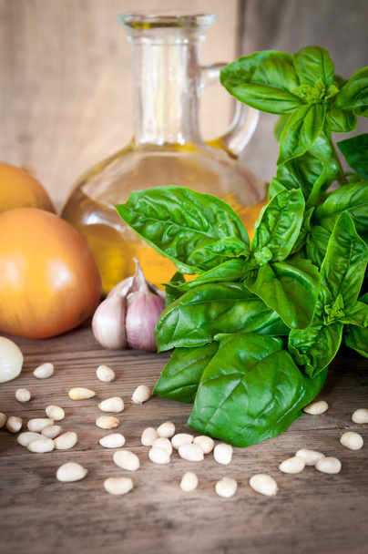 Fresh, green, organic basil on a wooden table. And products for salad: tomatoes, garlic, pine nuts. Photo is made in a rustic style with a blurred background. - Fotó, kép