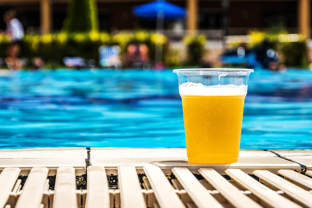Plastic bottle with draft beer in sunny day in summer near swimming pool - Φωτογραφία, εικόνα