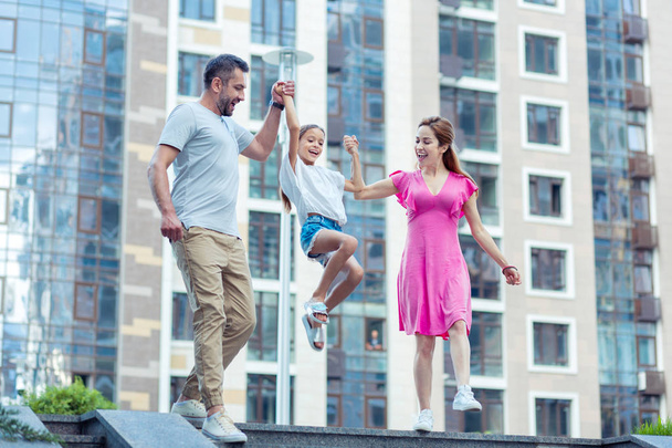 Happy nice girl jumping while holding her parents - Foto, Bild