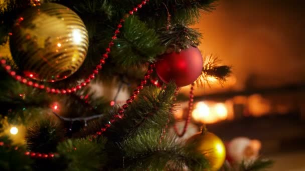 Closeup 4k video van mooi versierd kerstboom met rode en gouden kerstballen tegen de brandende open haard. Perfecte achtergrond voor winter feesten en feestdagen - Video