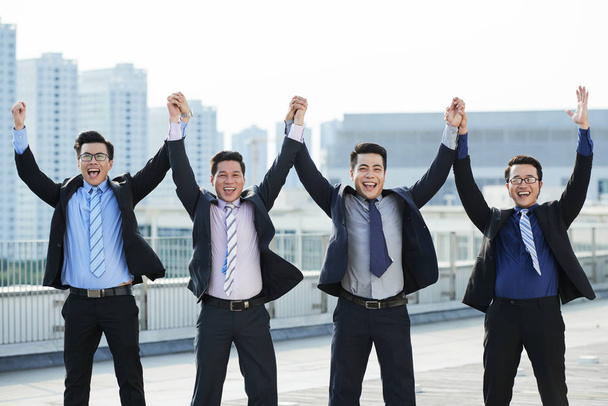 alegres gerentes asiáticos mirando a la cámara con sonrisas dentadas mientras celebran el éxito en el techo
  - Foto, imagen
