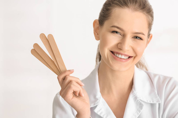 Kobiece kosmetolog gospodarstwa kije do depilacji na jasnym tle - Zdjęcie, obraz