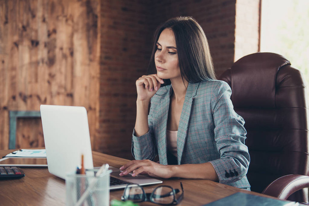 Stylish lovely professional, smart, beautiful latin lady wearing grey jacket, reading business letter in laptop, online meeting, sitting in armchair, modern loft work place, station - Фото, изображение