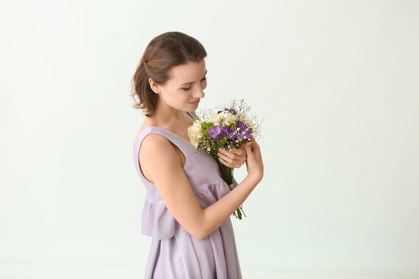 Beautiful woman with bouquet of flowers on light background - Foto, afbeelding