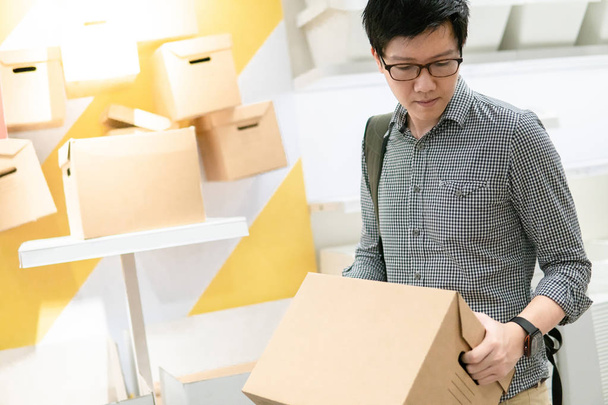 Joven hombre asiático llevando caja de cartón elegir qué comprar. concepto de compras de almacén
 - Foto, Imagen