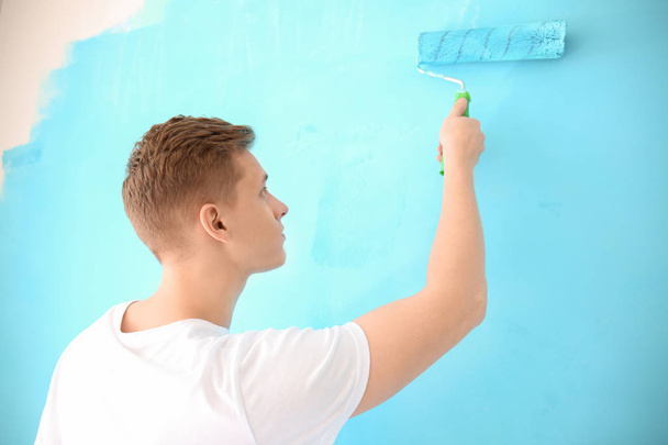 Male painter using roller for refurbishing color of wall indoors - Fotó, kép