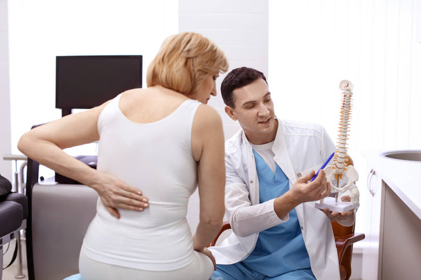 Orthopedist showing spine model to patient in hospital - Foto, afbeelding