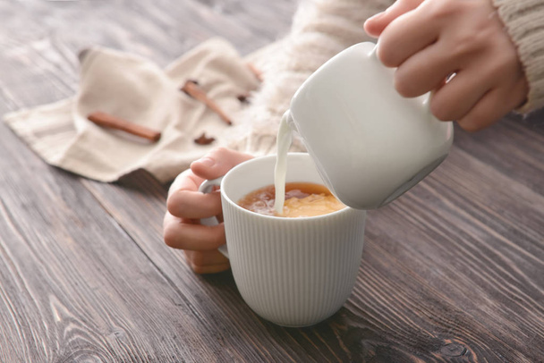 Mujer vertiendo leche en la taza de té en la mesa
 - Foto, Imagen