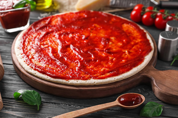 Pâte à pizza avec sauce tomate savoureuse sur table en bois
 - Photo, image