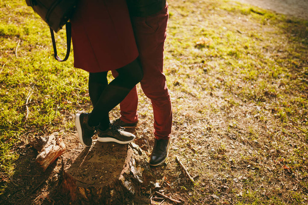Przycięte zdjęcie para młoda kobieta, mężczyzna w Burgundii ubrania kobiece, męskie nogi przytulanie Ogarnięcie stojący na Kikut w jesienny park miejski na zewnątrz w słoneczny dzień. Koncepcja styl życia rodziny relacji miłości - Zdjęcie, obraz