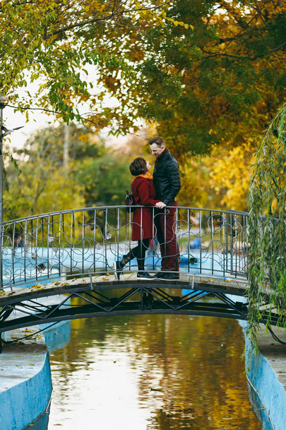 Młoda para romantyczne dama, człowiek w ciepłe ubrania ogarnięcie, patrząc na siebie, stojący w pobliżu staw na most w Jesień city park na zewnątrz. Miłości relacji rodziny osób lifestyle concept - Zdjęcie, obraz