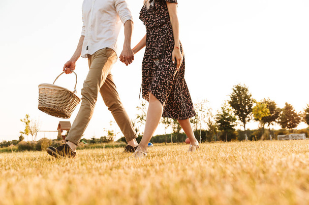 Cropped image of young couple with basket of drinks and food going to have picnic outdoors. - Foto, Imagem
