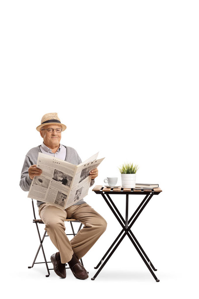 Elderly man sitting at a coffee table holding a newspaper isolated on white background - Foto, imagen