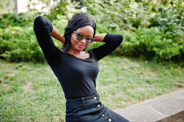 African american girl in sunglasses, black clothes and shirt sitting outdoor. Fashionable black woman. - Foto, Imagen