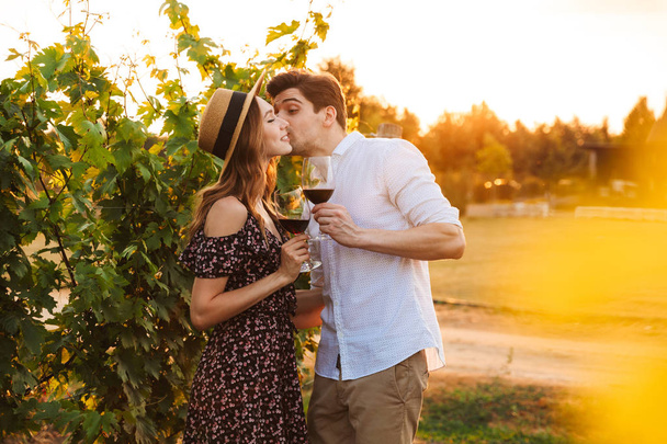 Photo of young cute happy loving couple outdoors drinking wine kissing. - Foto, Imagen