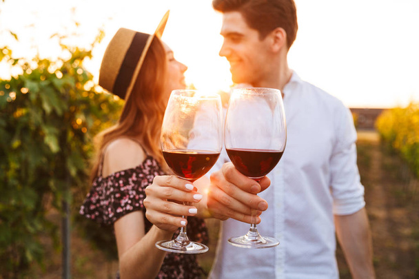 Photo of young cute happy loving couple outdoors drinking wine. Focus on glasses. - Foto, imagen