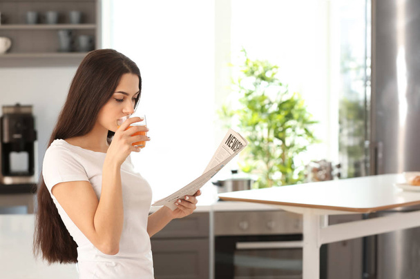 Молодая женщина читает газеты во время питья сока на кухне
 - Фото, изображение