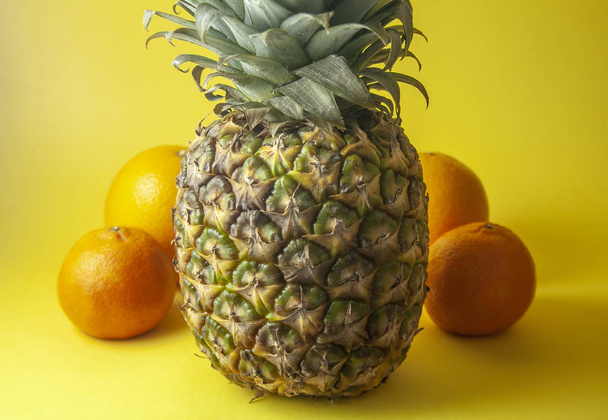 Pineapple isolated on yellow background with oranges and mandarin oranges. Shallow dof. - Fotó, kép