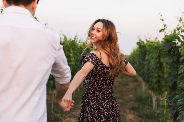 Romantic beautiful couple man and woman dating while walking outdoor together through vineyard on summer day - Photo, image