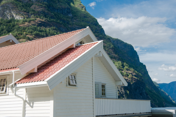 white wooden house with red roof near beautiful mountains at Aurlandsfjord, Flam (Aurlandsfjorden), Norway - Photo, Image