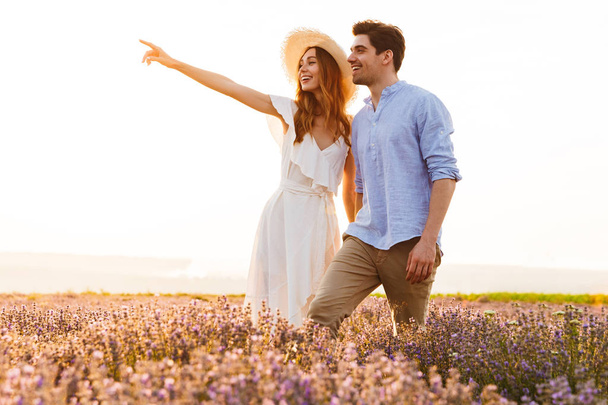 Happy young couple embracing at the lavender field, pointing finger - Fotoğraf, Görsel