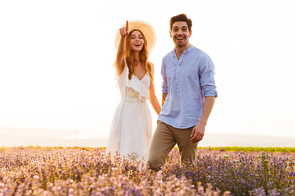 Lovely young couple embracing at the lavender field, pointing finger - Foto, Imagen