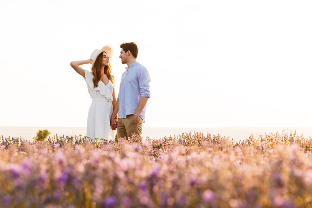 Photo of beautiful young people dating and walking together outdoor in lavender field - Zdjęcie, obraz