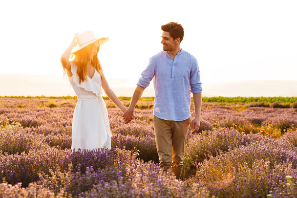 Photo of romantic young man and woman walking together outdoor in lavender field - Foto, afbeelding