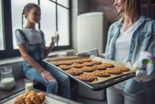 Mom and daughter in kitchen at home, woman is holding a sheet pan with freshly baked cookies - Photo, Image