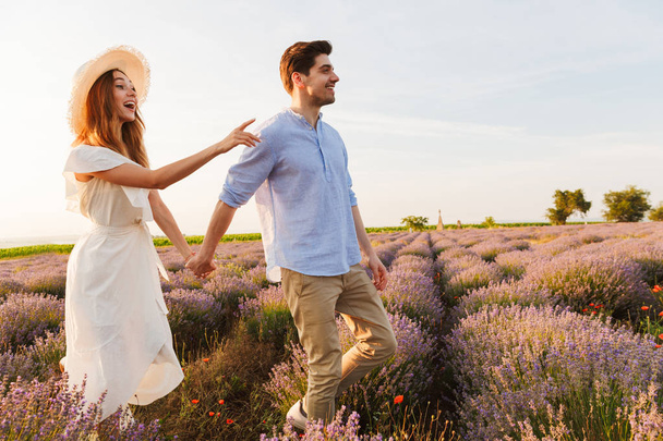 Photo of joyful young couple man and woman dating and walking outdoor in lavender field - Foto, immagini