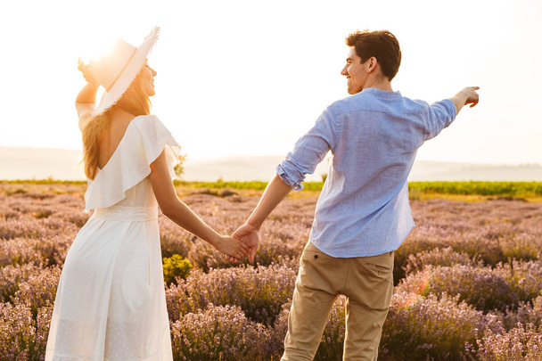 Happy young couple embracing at the lavender field, pointing finger - Foto, immagini