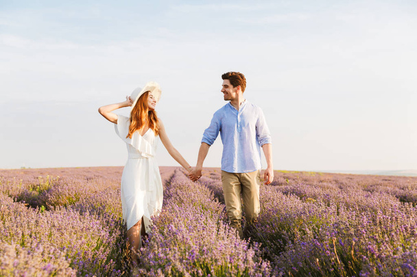 Cheery young couple embracing at the lavender field, holding hands, walking - Photo, Image