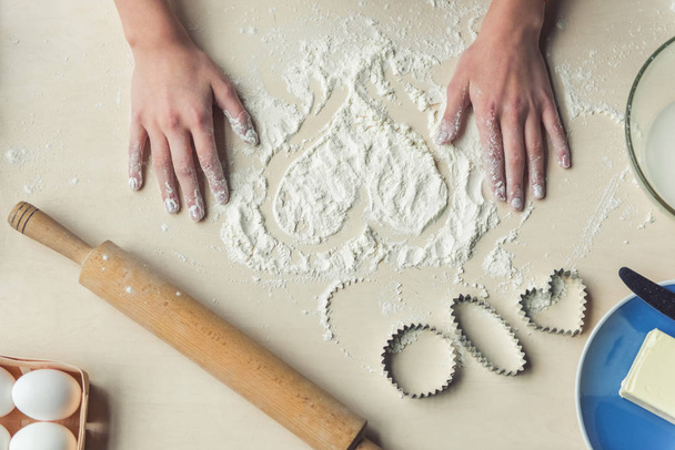 Imagen recortada, vista superior de la niña haciendo corazón de harina mientras hornea
 - Foto, Imagen