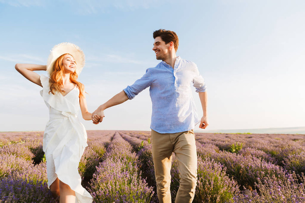 Cheerful young couple embracing at the lavender field, holding hands, running - Фото, зображення