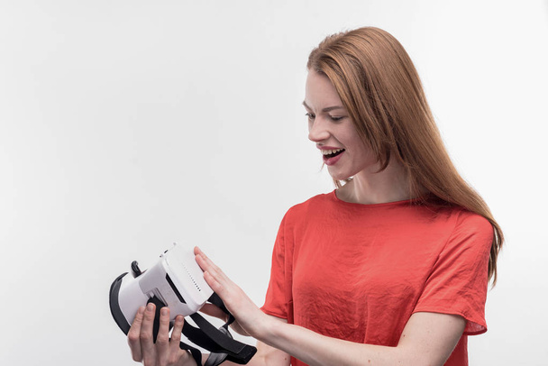 Young beaming woman feeling excited while holding virtual reality glasses - Photo, image