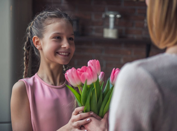 Kislány ad virágok, hogy az anyja, és mosolyogva, miközben állandó otthon a konyhában - Fotó, kép