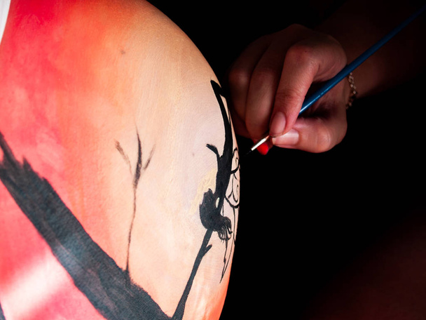 Female artist painting the belly of a pregnant young woman with body paints and brushes - Photo, Image