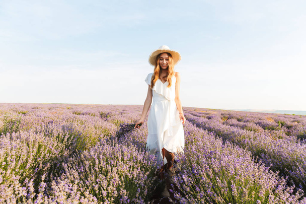 Smiling pretty young girl in straw hat walking at the lavender field - Fotoğraf, Görsel