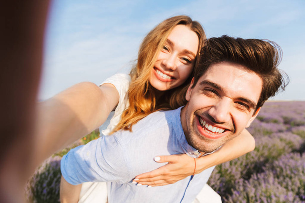 Happy young couple taking a selfie at the lavender field, piggyback ride - Foto, imagen